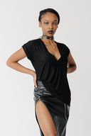 Front view of model wearing the Void Tee, a black jersey V-neck tee with a draped asymmetric hem, styled with a leather skirt sold separately