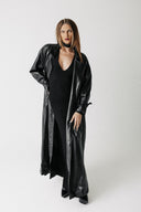 Front view of model wearing the Eclipse Trench, an oversized floor length cactus leather trench coat, open over a black dress
