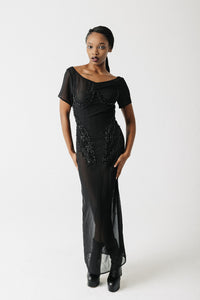 Model wearing black hand-beaded sheer chiffon gown, full length, with platform boots